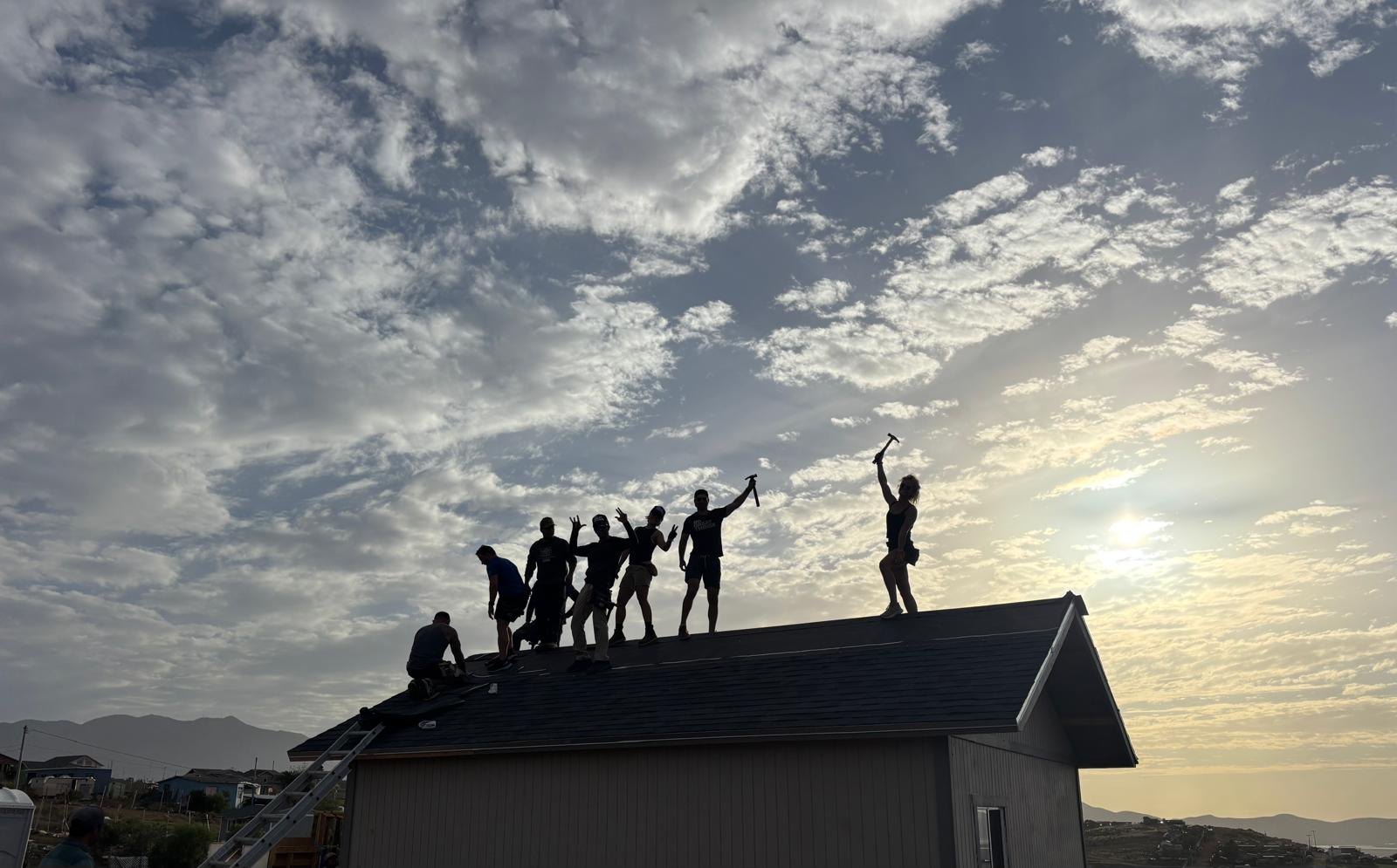 Adult volunteer crew celebrates together on the roof beneath a cloudy sky