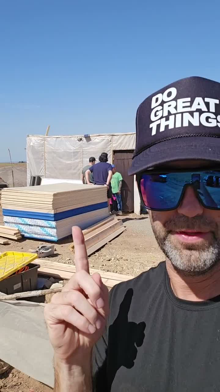 Volunteer in sunglasses points toward stacked building panels at the work site